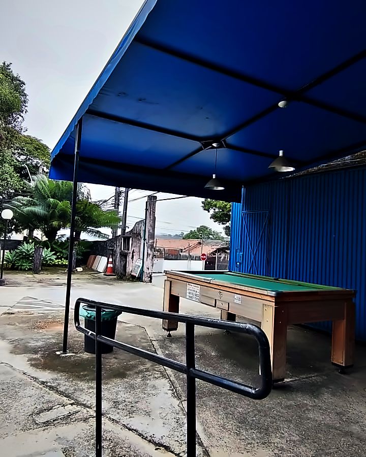 O pátio coberto por uma tenda azul, com a mesa de sinuca e o corrimão